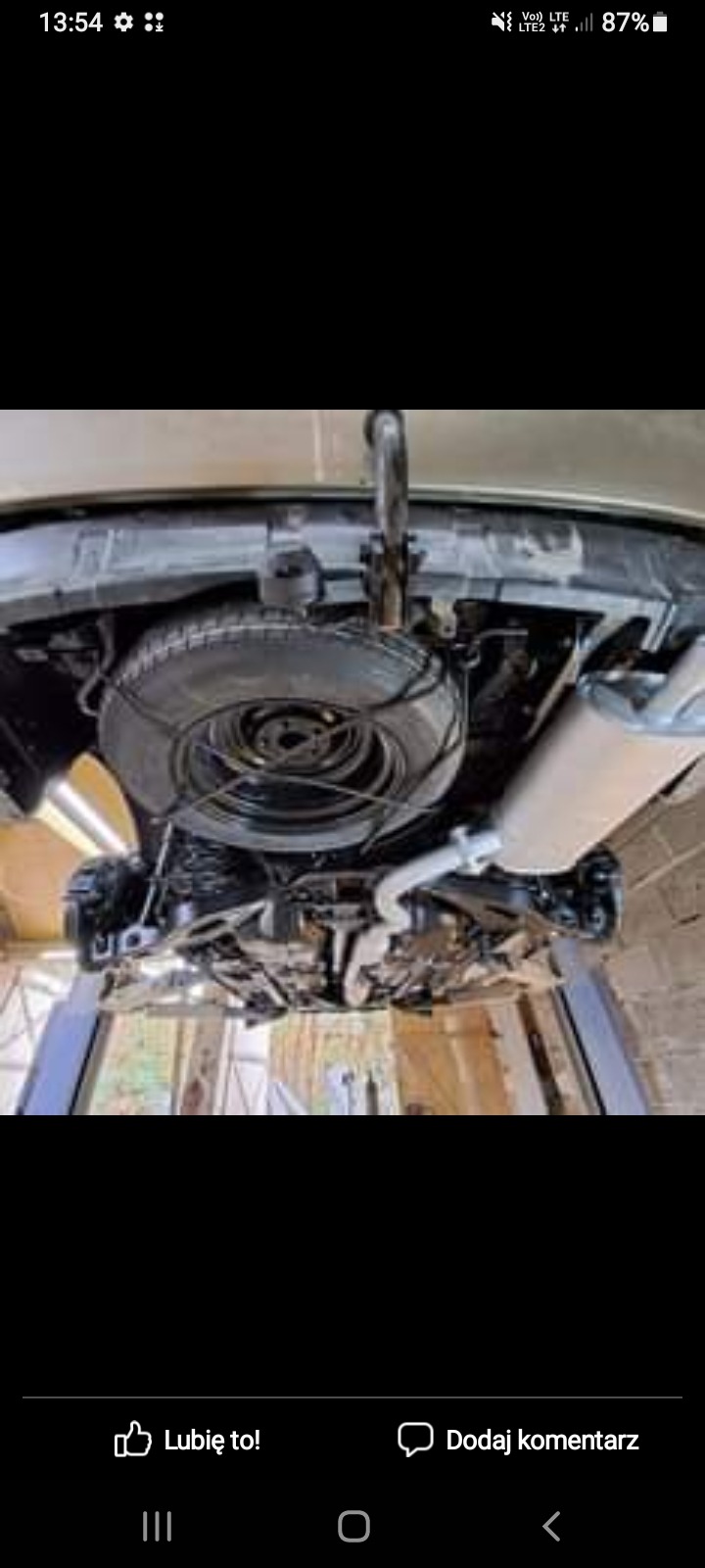 Podwozie samochodu na podnośniku, widoczne elementy zawieszenia, koło zapasowe i układ wydechowy po zabiegach konserwacyjnych.