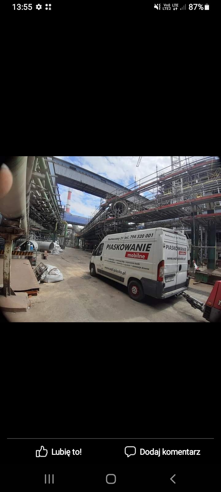 Biały samochód dostawczy z napisem 'PIASKOWANIE mobilne' zaparkowany na terenie przemysłowym, w tle widoczne rusztowania i rury instalacji przemysłowej.