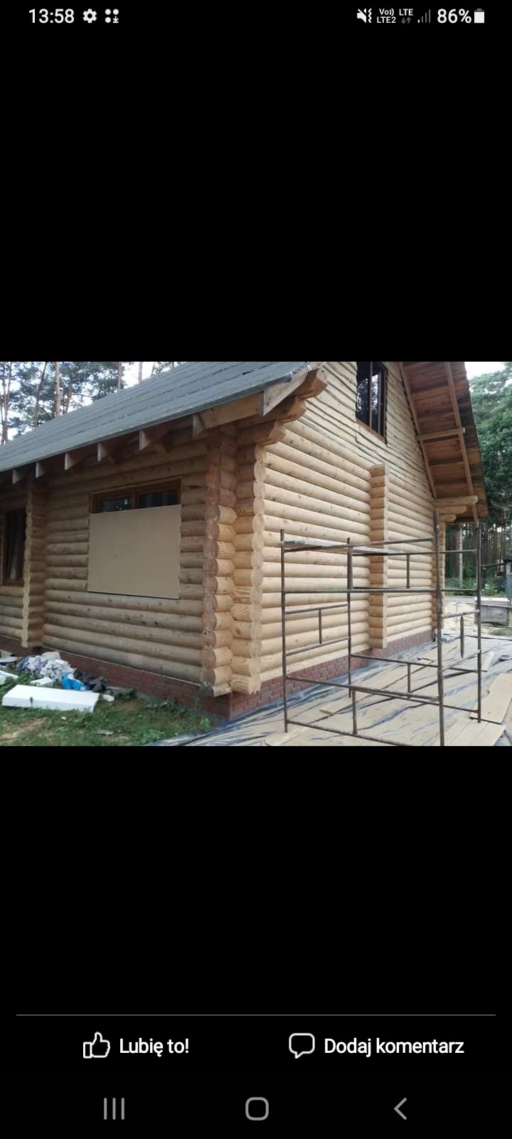 Drewniany dom z bali w trakcie budowy, z widocznym rusztowaniem i zabezpieczonymi oknami.