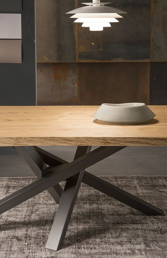 Blat drewniany z widoczną strukturą drewna, oparty na metalowej podstawie w kształcie gwiazdy, oświetlony nowoczesną lampą wiszącą. Na blacie ceramiczna misa.