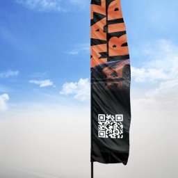 Daria Yanovich - Wysoki, czarny, reklamowy beachflag z pomarańczowym napisem 'MAKE RIDE' i zdjęciem sportowego samochodu oraz kodem QR, ustawiony na tle błękitnego nieba z chmurami i szarej drogi.