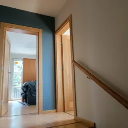 Korytarz po remoncie z dwoma otwartymi drewnianymi drzwiami, ściany pomalowane na szaro i ciemny niebieski, widoczna drewniana balustrada schodów.