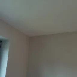 Pomieszczenie po malowaniu z widocznym fragmentem okna, jasne ściany i sufit w odcieniach beżu i szarości.