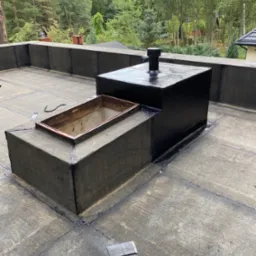 Wykończony płaski dach pokryty papą termozgrzewalną z kominkiem wentylacyjnym i wyłazem dachowym, widoczne łączenia i fragmenty papy na powierzchni.