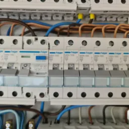 Rozdzielnica elektryczna Hager z zainstalowanymi bezpiecznikami topikowymi i wyłącznikiem r&oacute;żnicowoprądowym, widoczne kable w r&oacute;żnych kolorach i oznaczenia na urządzeniach.