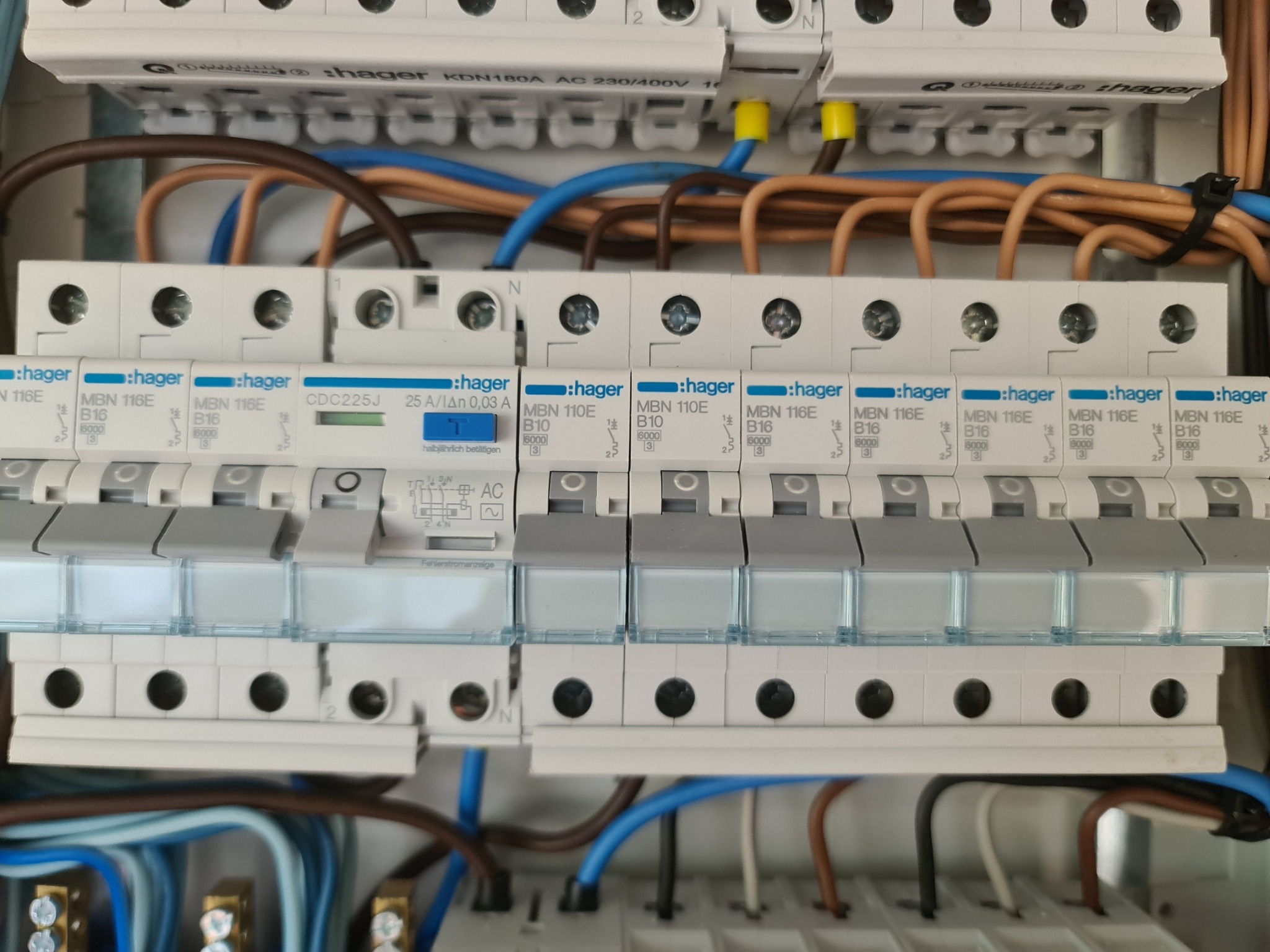 Rozdzielnica elektryczna Hager z zainstalowanymi bezpiecznikami topikowymi i wyłącznikiem różnicowoprądowym, widoczne kable w różnych kolorach i oznaczenia na urządzeniach.