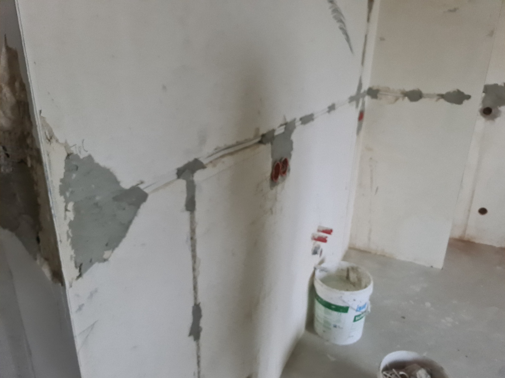 Ściana w trakcie montażu instalacji elektrycznej: widoczne kable w peszlach, puszki pod gniazdka zalewane gipsem, surowe wykończenie.