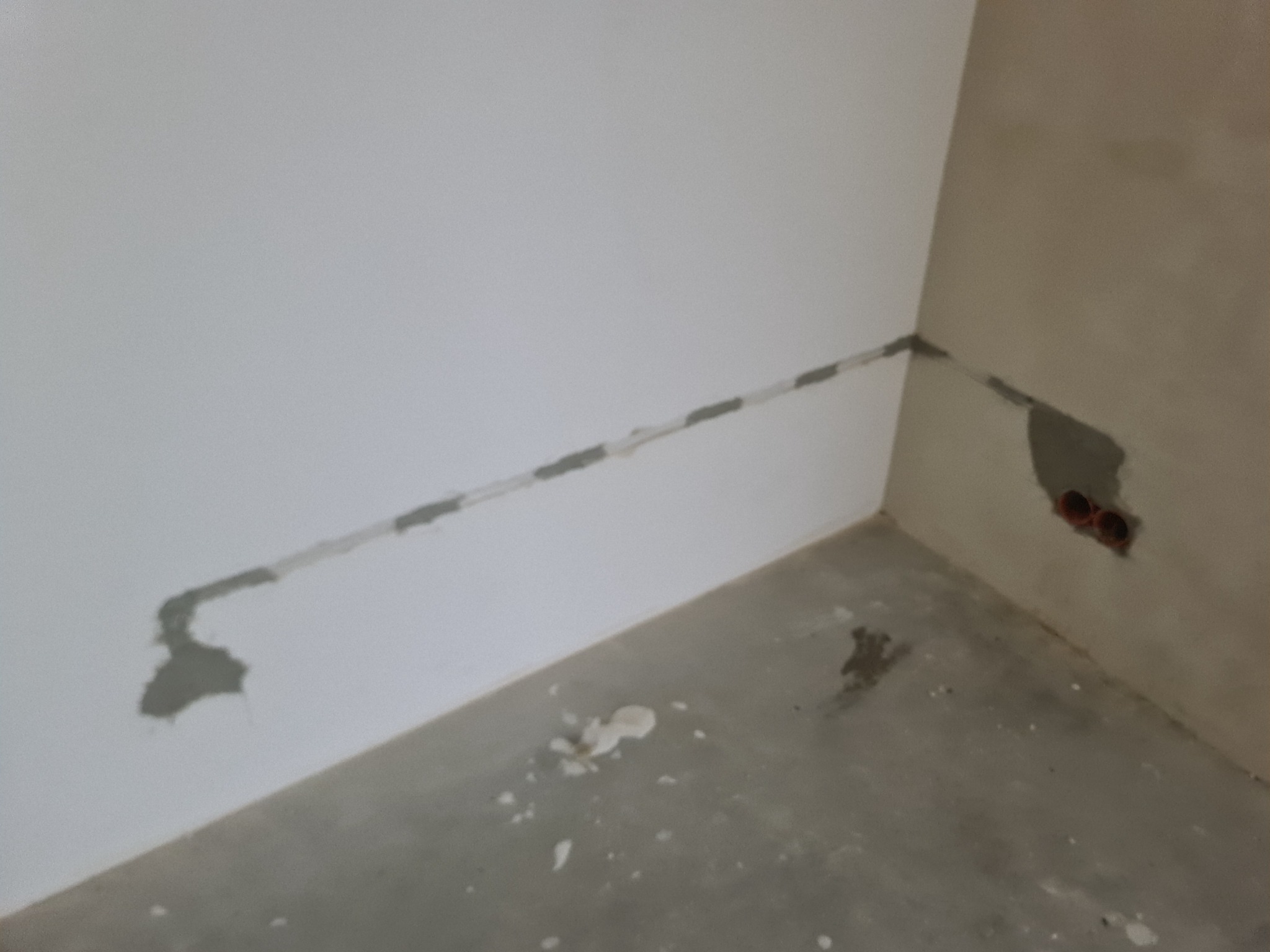 Bruzdowanie pod przewody elektryczne w ścianie, widoczne ślady po frezowaniu i gipsowaniu, surowy stan wykończenia wnętrza.