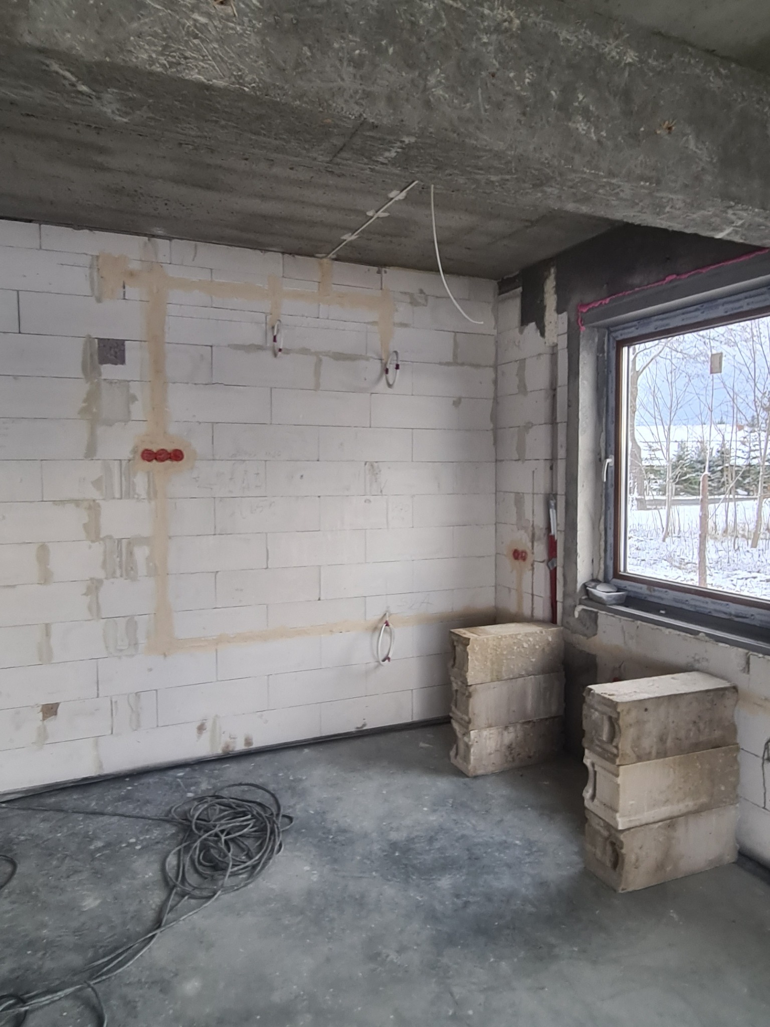 Surowy stan wnętrza z widoczną instalacją elektryczną w bruzdach na ścianie z betonu komórkowego, przygotowanego do dalszych prac wykończeniowych.
