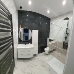 Nowoczesna łazienka z czarnymi i białymi marmurkowymi płytkami, białą armaturą, grzejnikiem drabinkowym i okrągłym lustrem z oświetleniem.