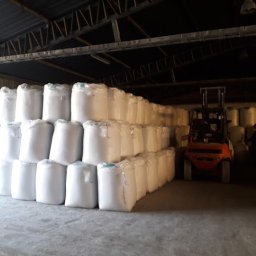 P.P.H.U Prohaus - Magazyn z rzędami ułożonych worków z białego tworzywa, w tle wózek widłowy i sylwetka osoby.