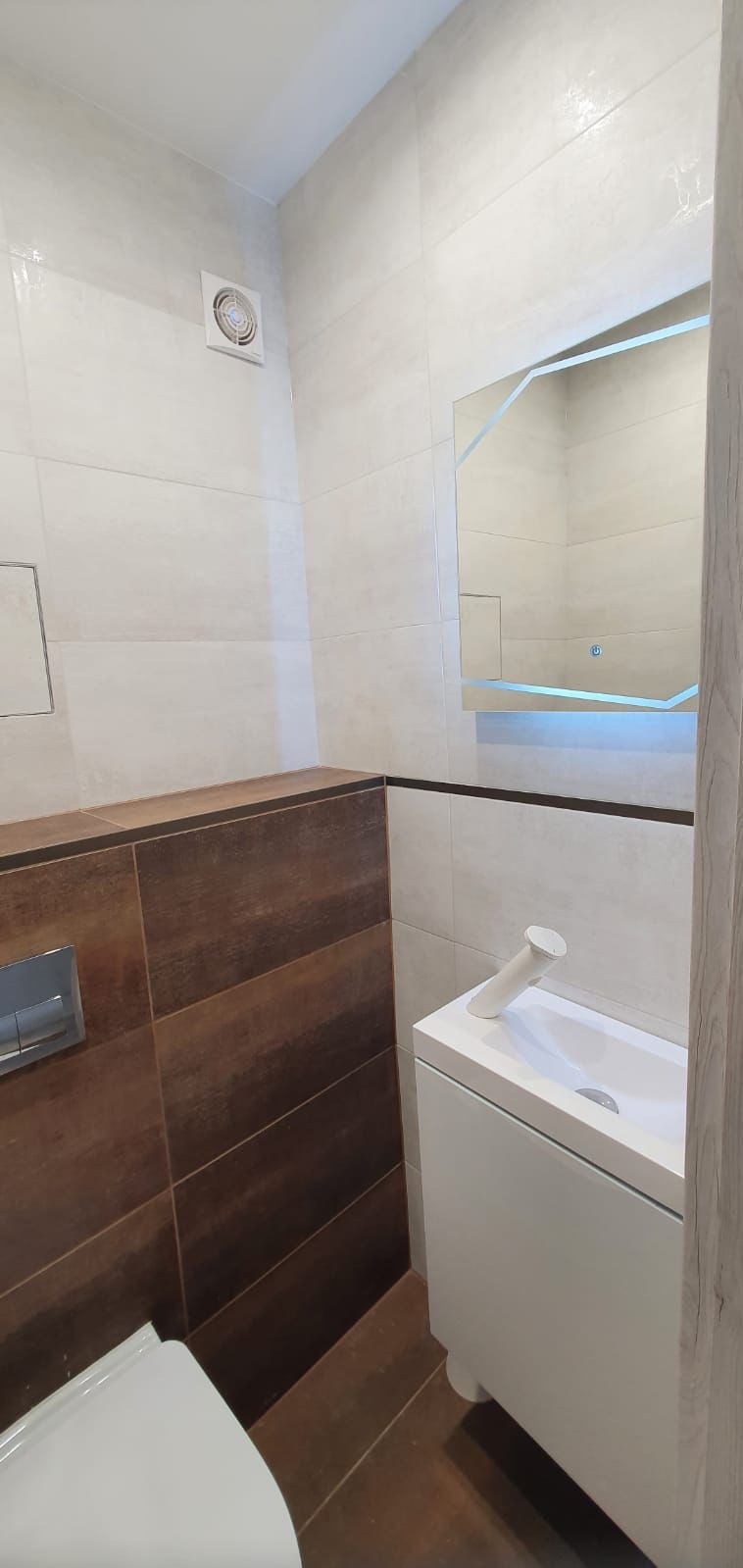 Nowoczesna łazienka z umywalką nablatową, podświetlanym lustrem o nieregularnym kształcie i brązowo-beżowymi płytkami na ścianach.