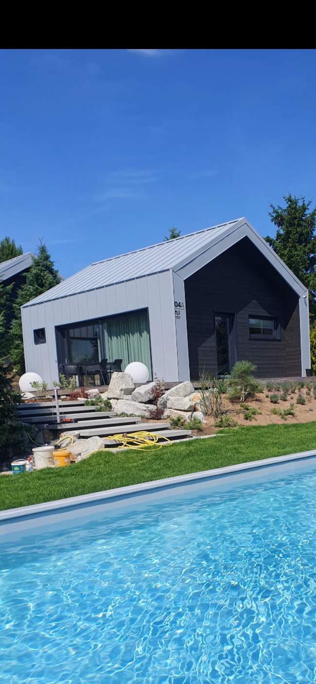 Nowoczesny, dwukolorowy dom z szarymi oknami i drzwiami przesuwnymi, widok z perspektywy basenu, z widocznymi schodami prowadzącymi do wejścia, elementami dekoracyjnymi i narzędziami malarskimi.