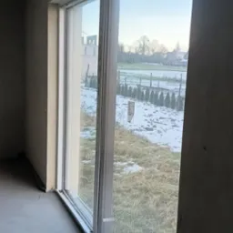 Surowe ściany wewnętrzne z oknem na zewnątrz, gdzie widać częściowo ośnieżony krajobraz.