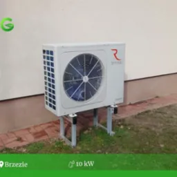 Zewnętrzna jednostka pompy ciepła Rotenso Aquami 10kW zamontowana na metalowych wspornikach przy elewacji budynku z widocznym logo firmy.
