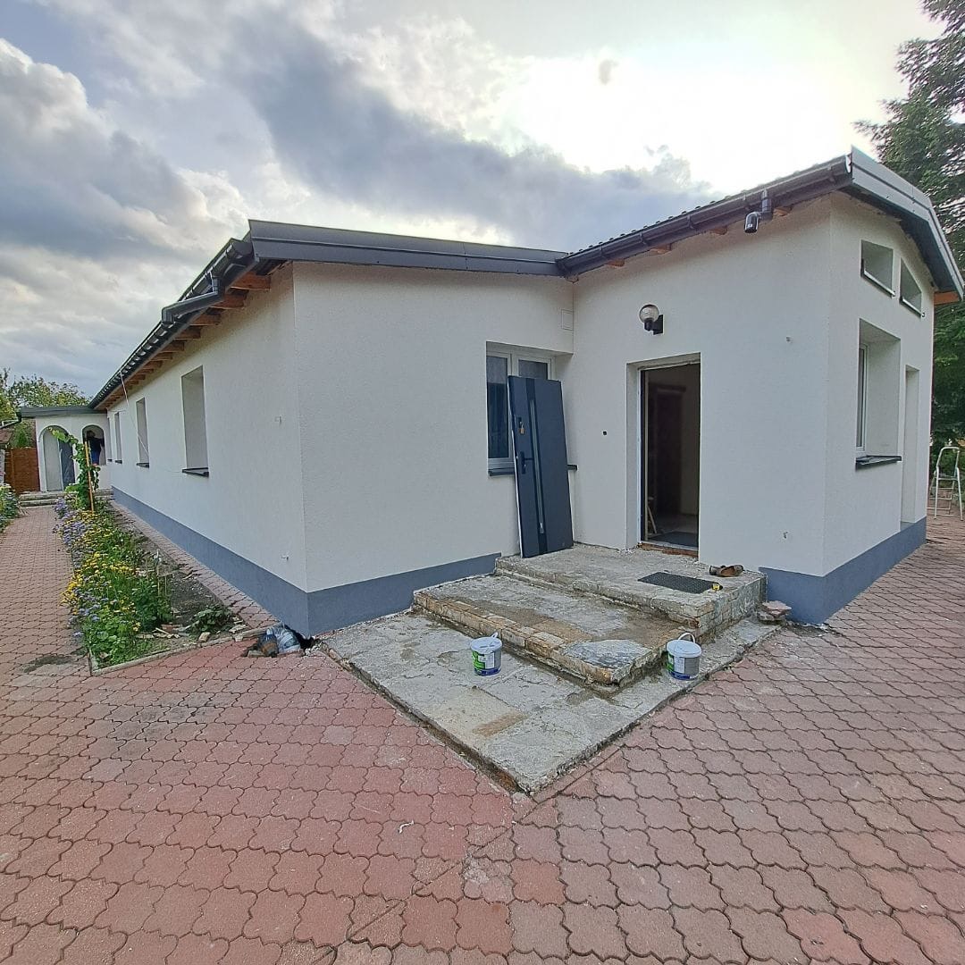 Dom jednorodzinny po ociepleniu elewacji, widoczne dwa wiadra z farbą na schodach wejściowych i niedokończone wykończenie cokołu.