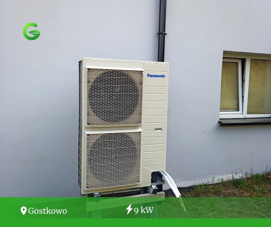 Zewnętrzna jednostka pompy ciepła Panasonic o mocy 9kW zamontowana na szarej ścianie budynku z widocznym oknem i rurami odprowadzającymi skropliny.