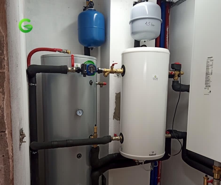 Dwa zbiorniki akumulacyjne ciepła: szary z manometrem i czerwonym zaworem oraz biały z szarą membraną, połączone rurami w kotłowni.