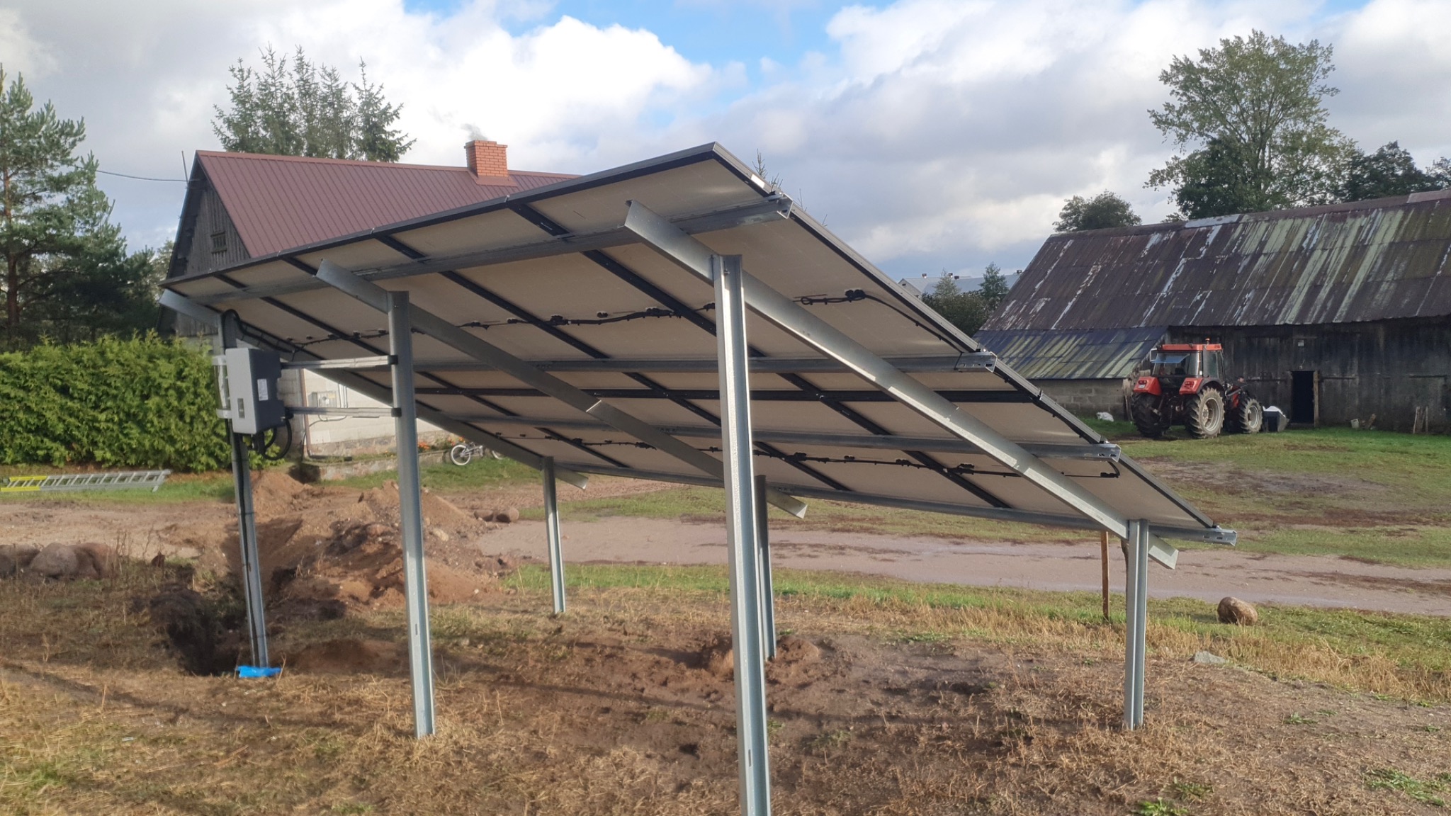 Montaż paneli słonecznych na stelażu z widocznym traktorem w tle, instalacja w trakcie prac ziemnych.