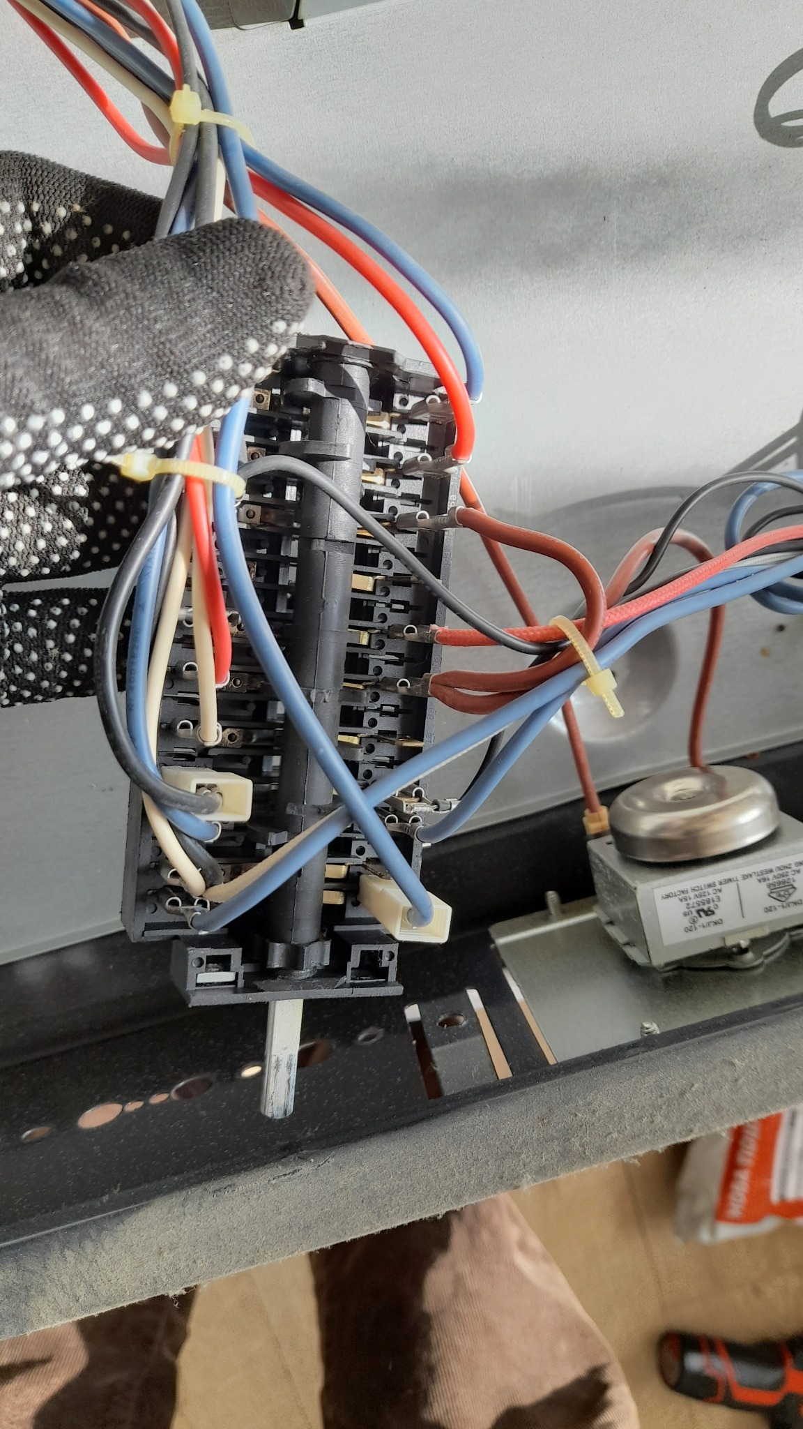 Elektryk w rękawicy w kropki podłącza przewody do bloku złącz wewnątrz urządzenia, widoczny timer i przewody spięte opaskami zaciskowymi.