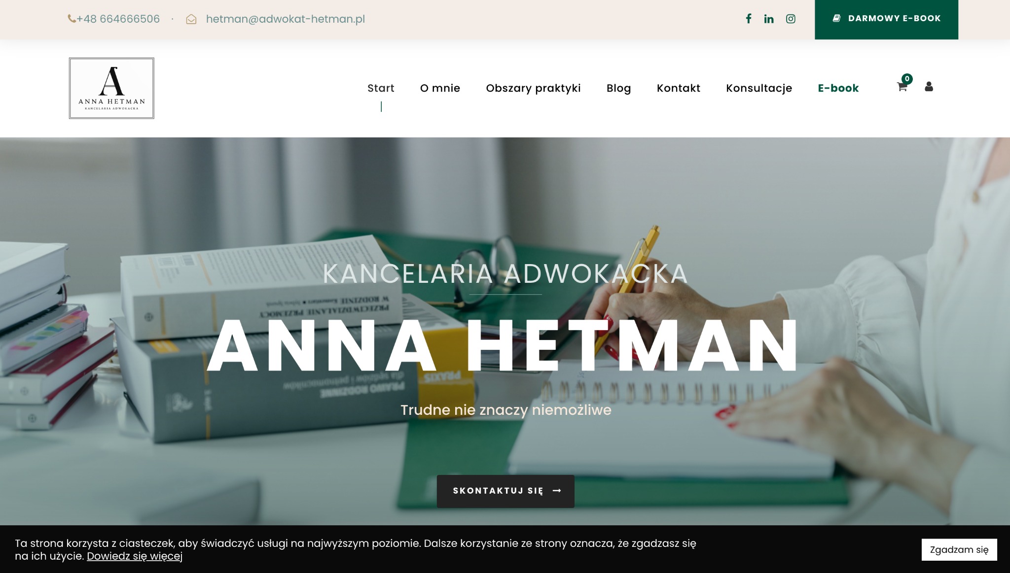 Strona internetowa kancelarii adwokackiej Anny Hetman z widocznym nagłówkiem, stosem książek prawniczych, okularami i dłonią piszącą w notatniku.