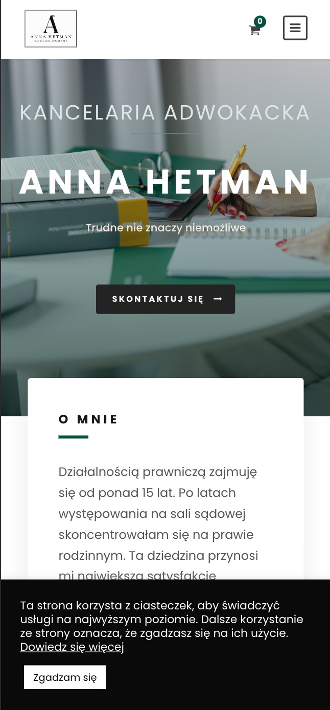 Fragment strony internetowej kancelarii adwokackiej Anna Hetman z widocznym logotypem, hasłem 'Trudne nie znaczy niemożliwe', dłonią piszącą na notatniku oraz stosem akt.