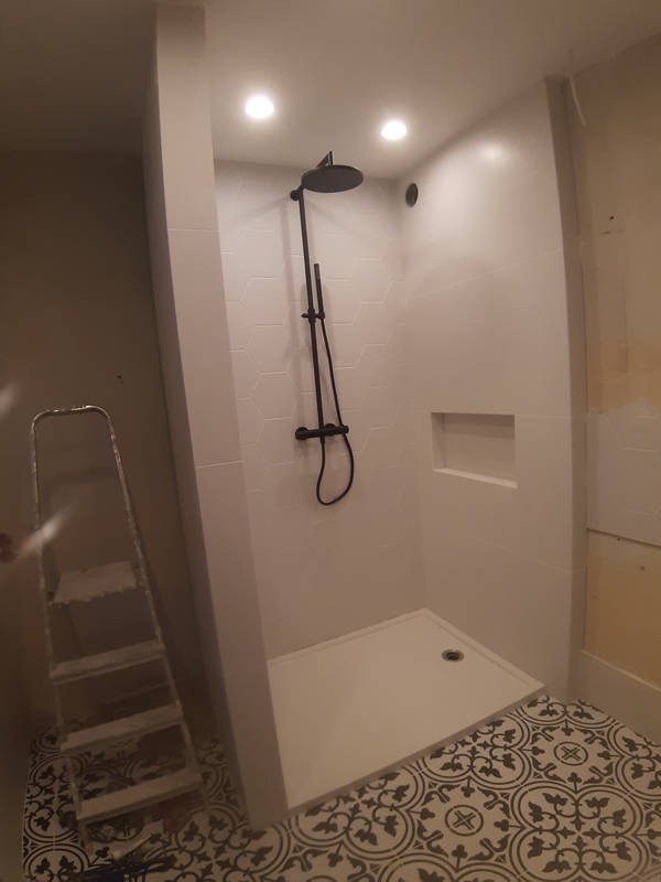 Nowoczesna kabina prysznicowa z czarną armaturą, heksagonalne płytki na ścianach i wzorzysta podłoga, drabina malarska w rogu.