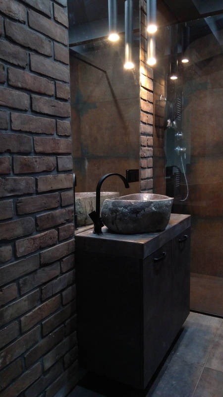 Industrialna łazienka z umywalką z naturalnego kamienia, czarną armaturą i ścianą z cegły, oświetlona wiszącymi lampami tubami.