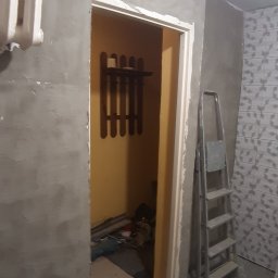 Osoba prywatna - Ściana w trakcie gruntowania pod malowanie, widoczna drabina, grzejnik i fragment wykończonej łazienki z płytkami wzorzystymi.