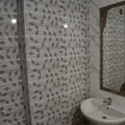 Nowoczesna łazienka z umywalką na postumencie, ściany wyłożone szaro-białymi płytkami z geometrycznym wzorem kostek, widoczny fragment lustra i kratka wentylacyjna.