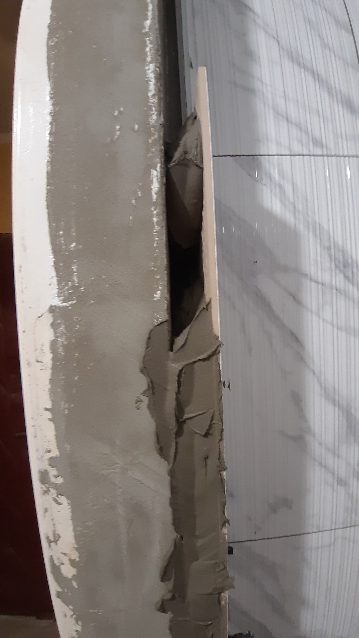 Nakładanie zaprawy murarskiej na ścianę z płytek, widoczna szpachelka i nierównomierne rozprowadzenie kleju.