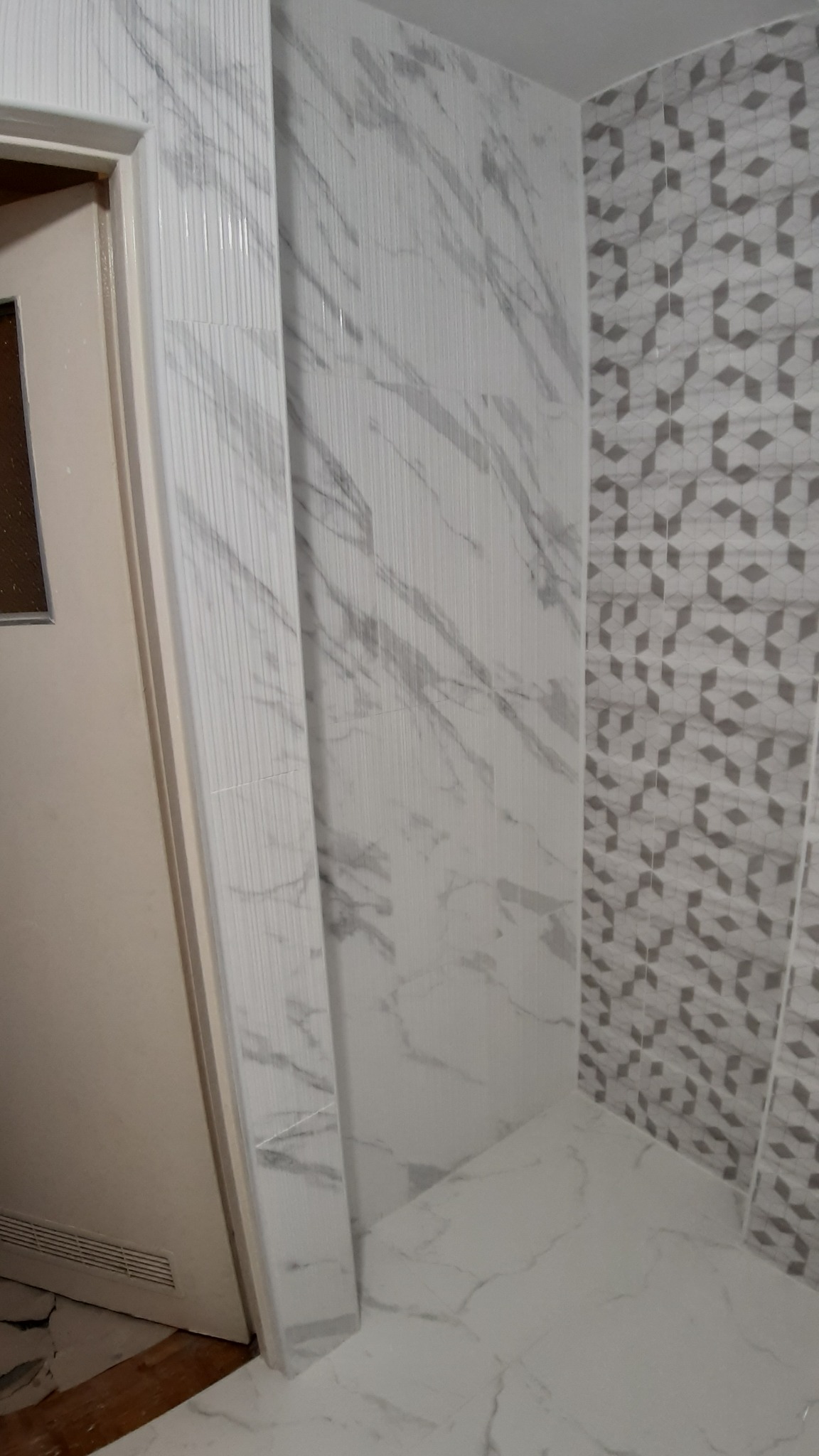 Wykończona łazienka z płytkami imitującymi marmur na ścianach i podłodze, wzór geometryczny na jednej ze ścian, widoczny fragment futryny drzwi.