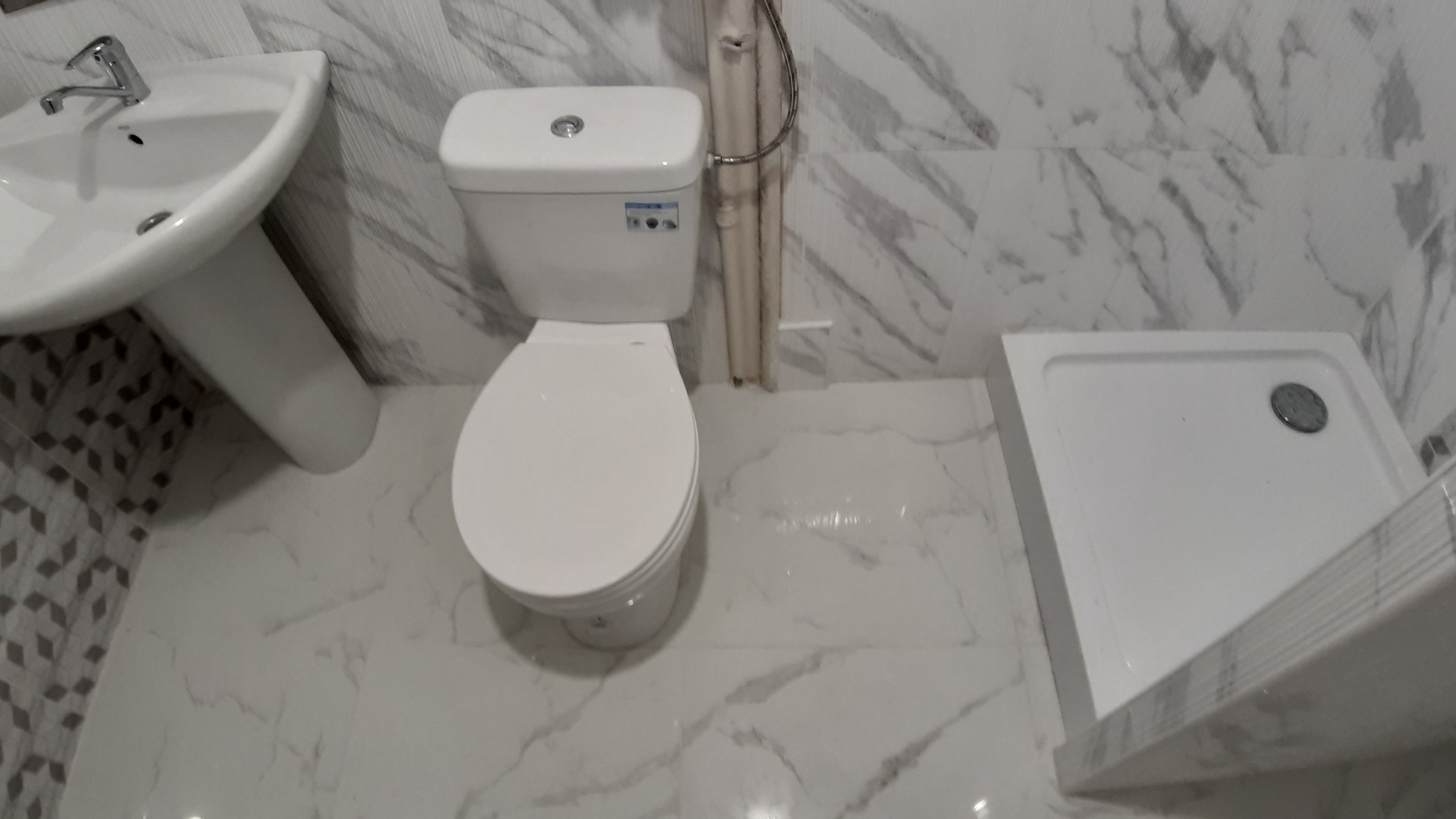 Wnętrze wykończonej łazienki z marmurową okładziną, widoczna umywalka na postumencie, toaleta i brodzik.