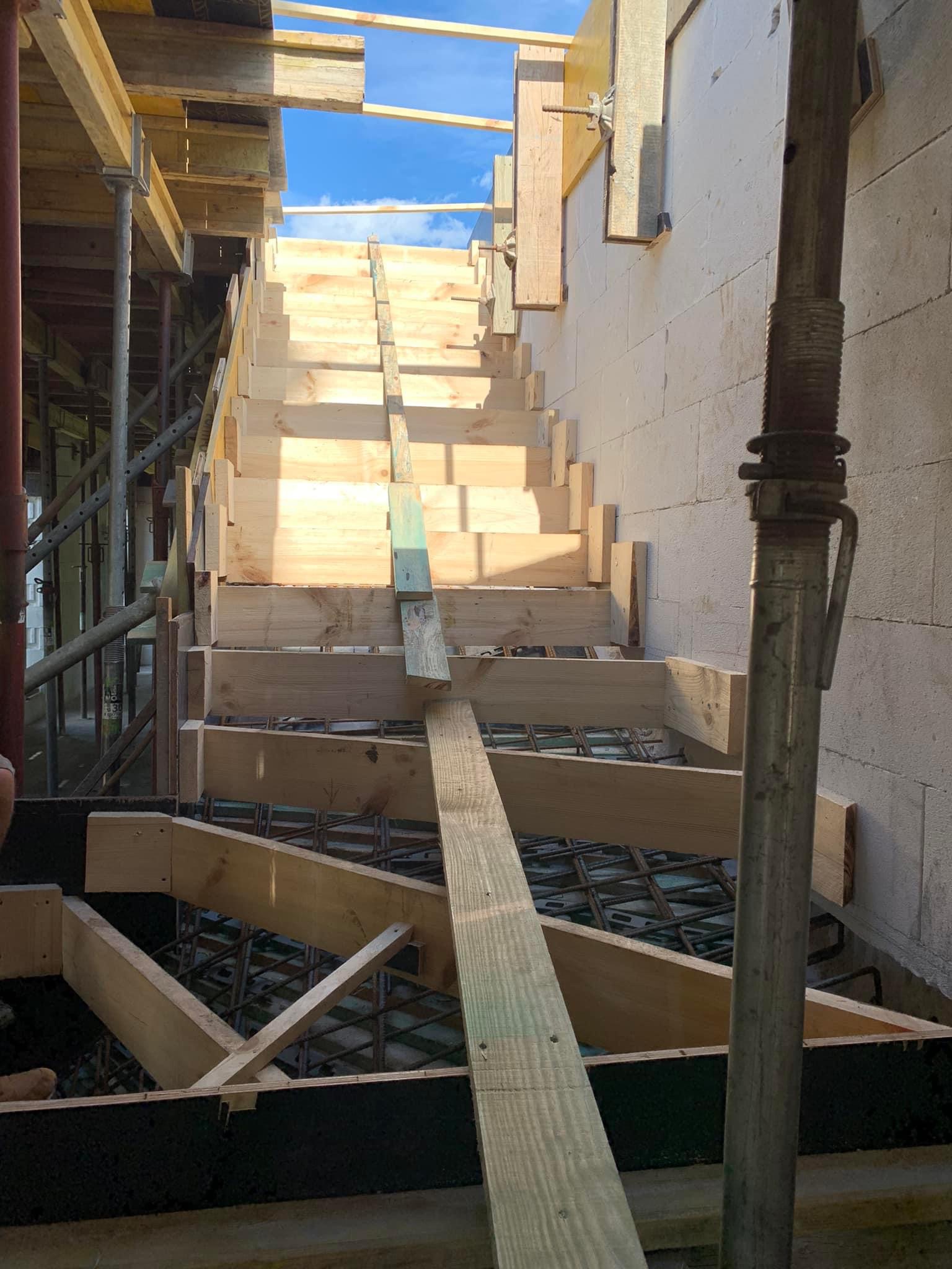 Szczegółowy widok drewnianego szalunku schodów w trakcie budowy domu z betonu komórkowego, widoczne zbrojenie i podpory montażowe.