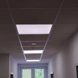 Korytarz biurowy z podwieszanym sufitem kasetonowym i wbudowanymi panelami LED, widok z dołu na sufit i drzwi na końcu korytarza.