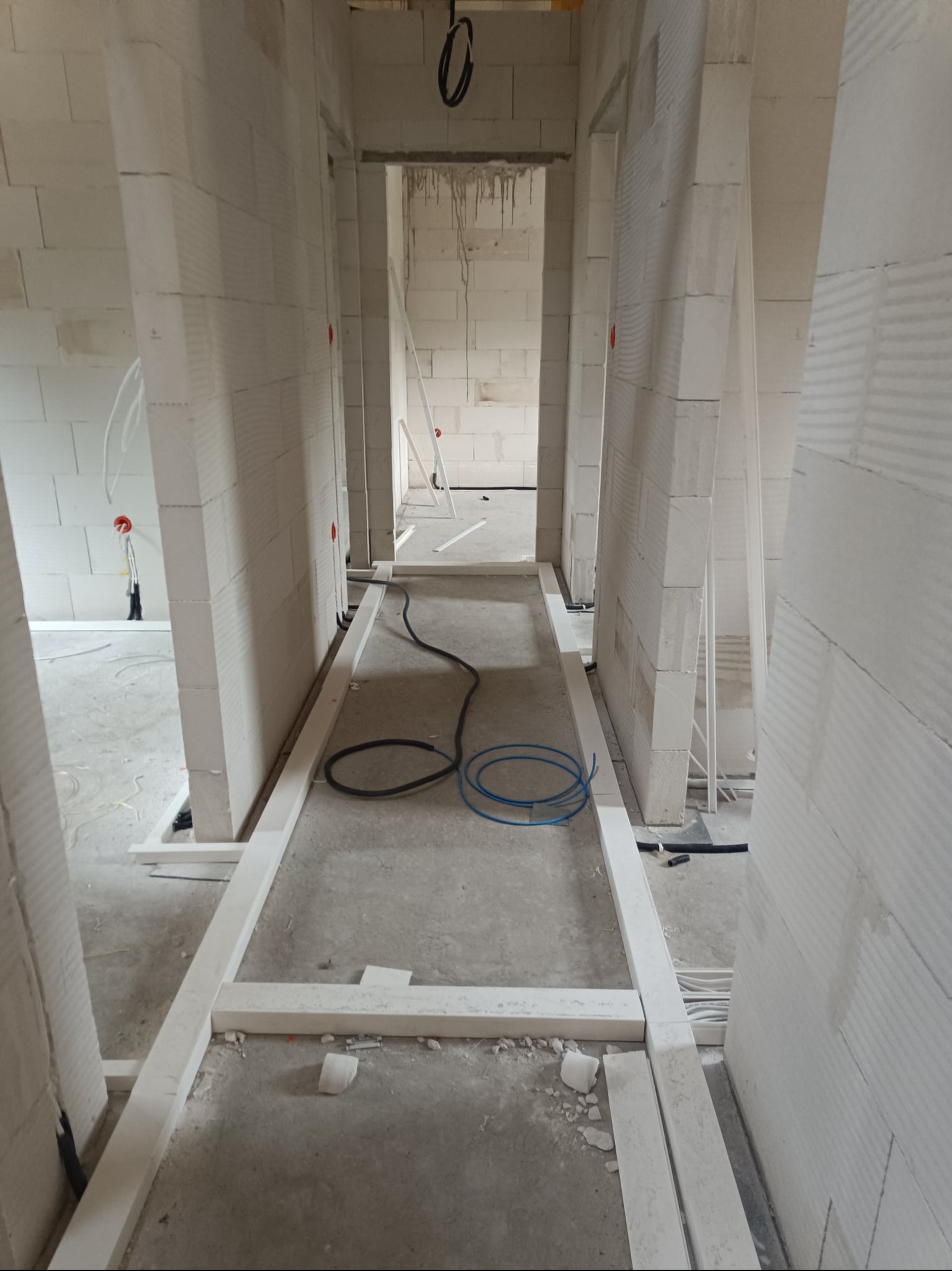 Wnętrze w trakcie budowy z widocznymi przewodami elektrycznymi na podłodze i w ścianach z białego betonu komórkowego.