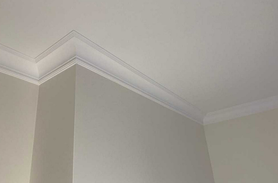 Wykończony narożnik pomieszczenia z listwami dekoracyjnymi przy suficie, widoczne łączenie listew pod kątem 90 stopni.