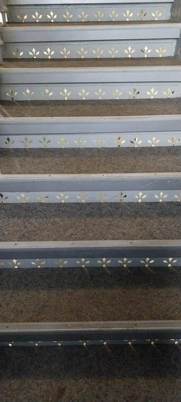 Szare schody z wykładziną i ozdobnymi, złotymi motywami roślinnymi na krawędziach stopni.