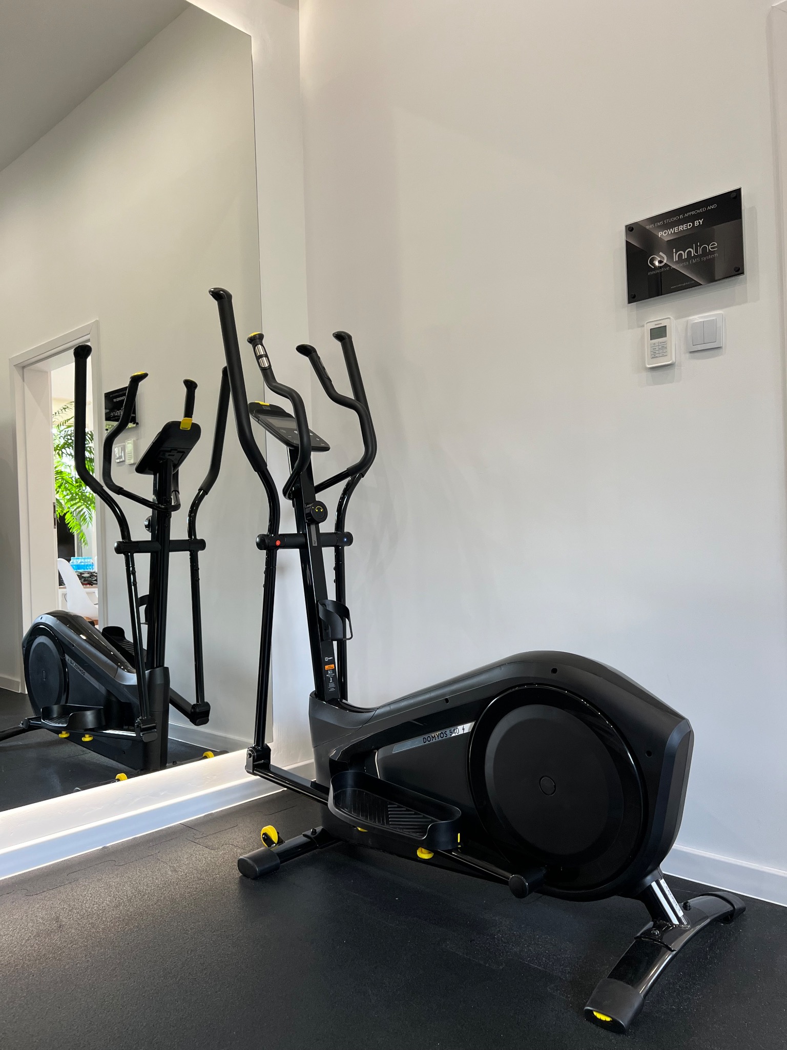 Czarny orbitrek Domynos 540 w jasnym pomieszczeniu z lustrem, widoczny znak 'Powered by Innline' na ścianie.