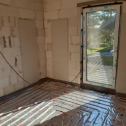 Instalacja ogrzewania podłogowego w surowym wnętrzu w Wyszkowie, rury grzewcze rozłożone na siatce, folia ochronna, widoczne okno z PCV.