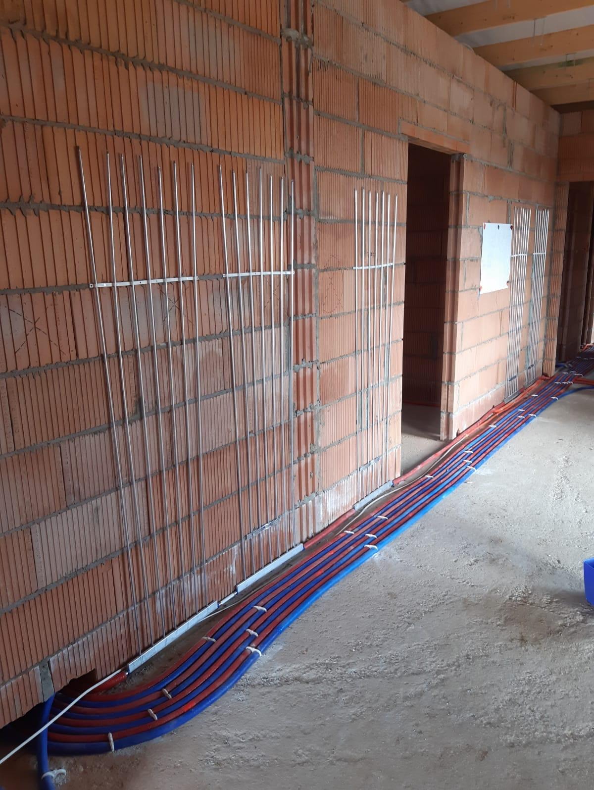 Instalacja rur ogrzewania podłogowego w surowym stanie, widoczne mocowania do ściany z pustaków ceramicznych, rury prowadzone wzdłuż ścian.