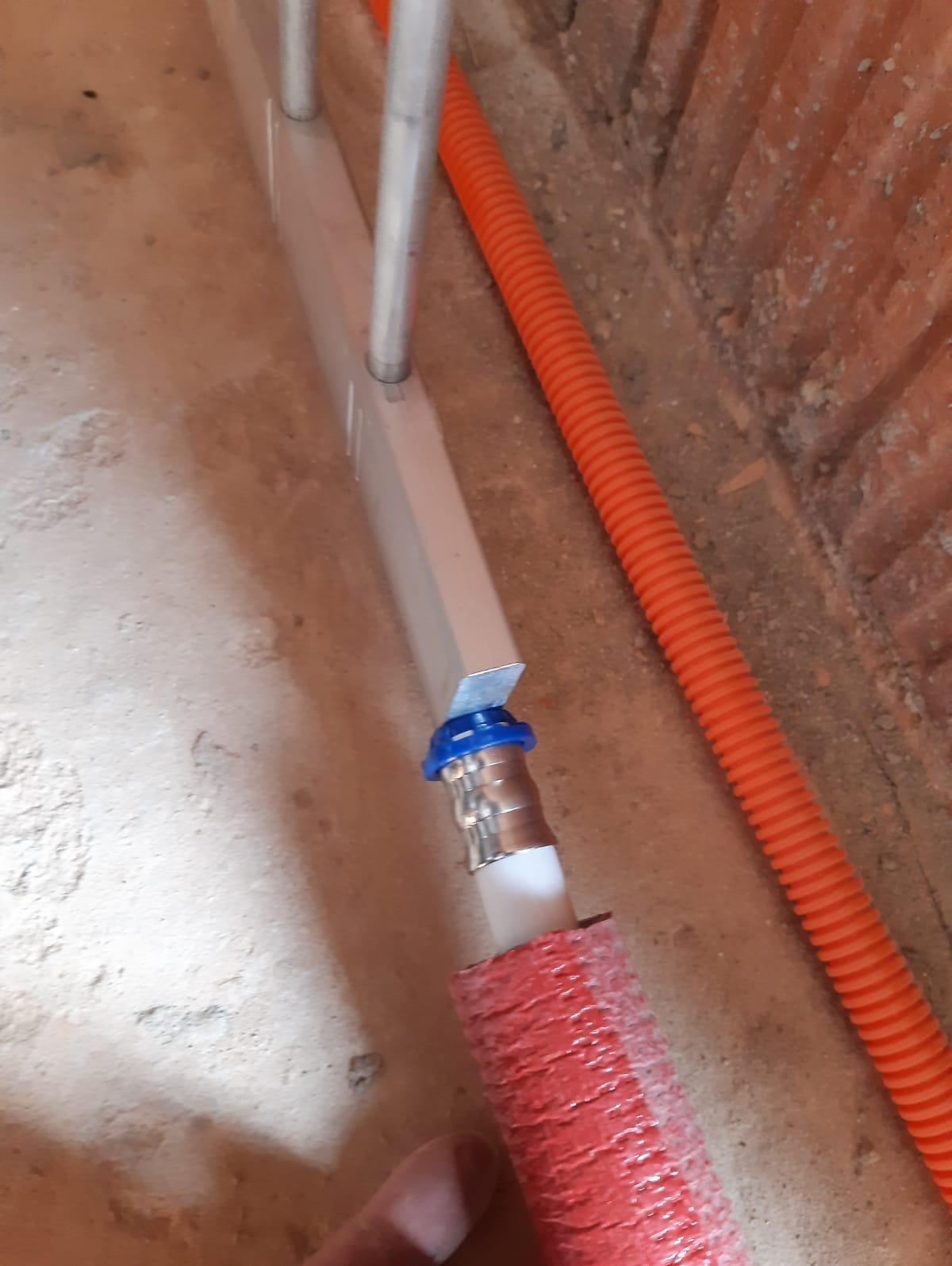 Rura grzewcza w izolacji, podłączona do grzejnika, z widoczną rurą karbowaną w tle, w trakcie montażu w surowym wnętrzu.