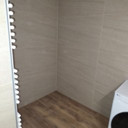 Drex - Beżowa łazienka z drewnopodobną podłogą, grzejnikiem drabinkowym i pralką LG. Płytki ścienne imitujące kamień. Minimalistyczny design.