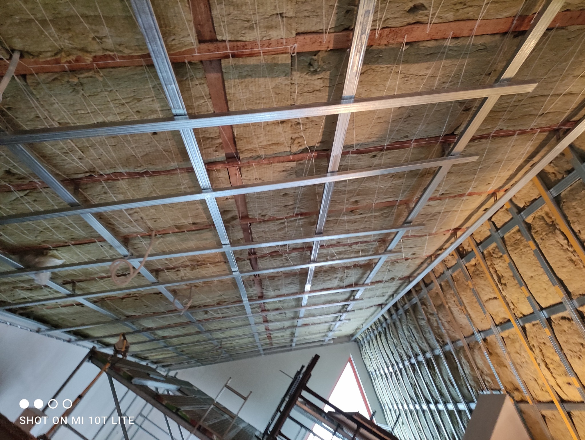 Montaż izolacji z wełny mineralnej i metalowej konstrukcji pod płytę karton-gips na poddaszu, widok z dołu na rusztowanie.