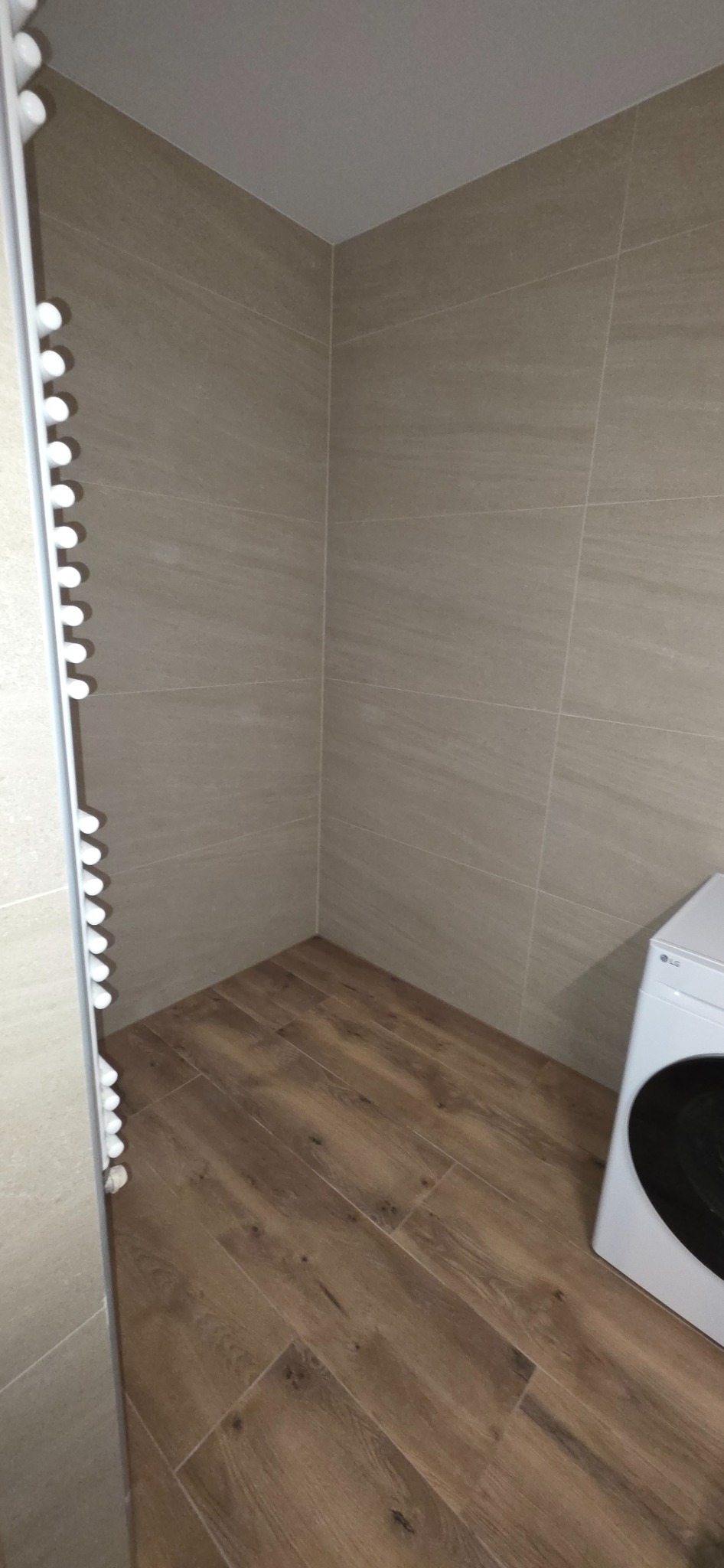 Beżowa łazienka z drewnopodobną podłogą, grzejnikiem drabinkowym i pralką LG. Płytki ścienne imitujące kamień. Minimalistyczny design.