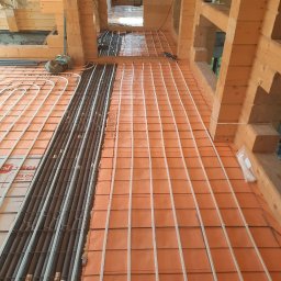 PREMIUM BUD SERHII HORDIICHUK - Montaż ogrzewania podłogowego: rury grzewcze ułożone na pomarańczowej izolacji termicznej, widoczne drewniane elementy konstrukcyjne domu w surowym stanie.