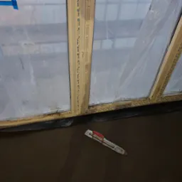 Świeżo wylana, ciemna podłoga zacierana pacą z czerwonym uchwytem, zabezpieczona folią i taśmą okienna.