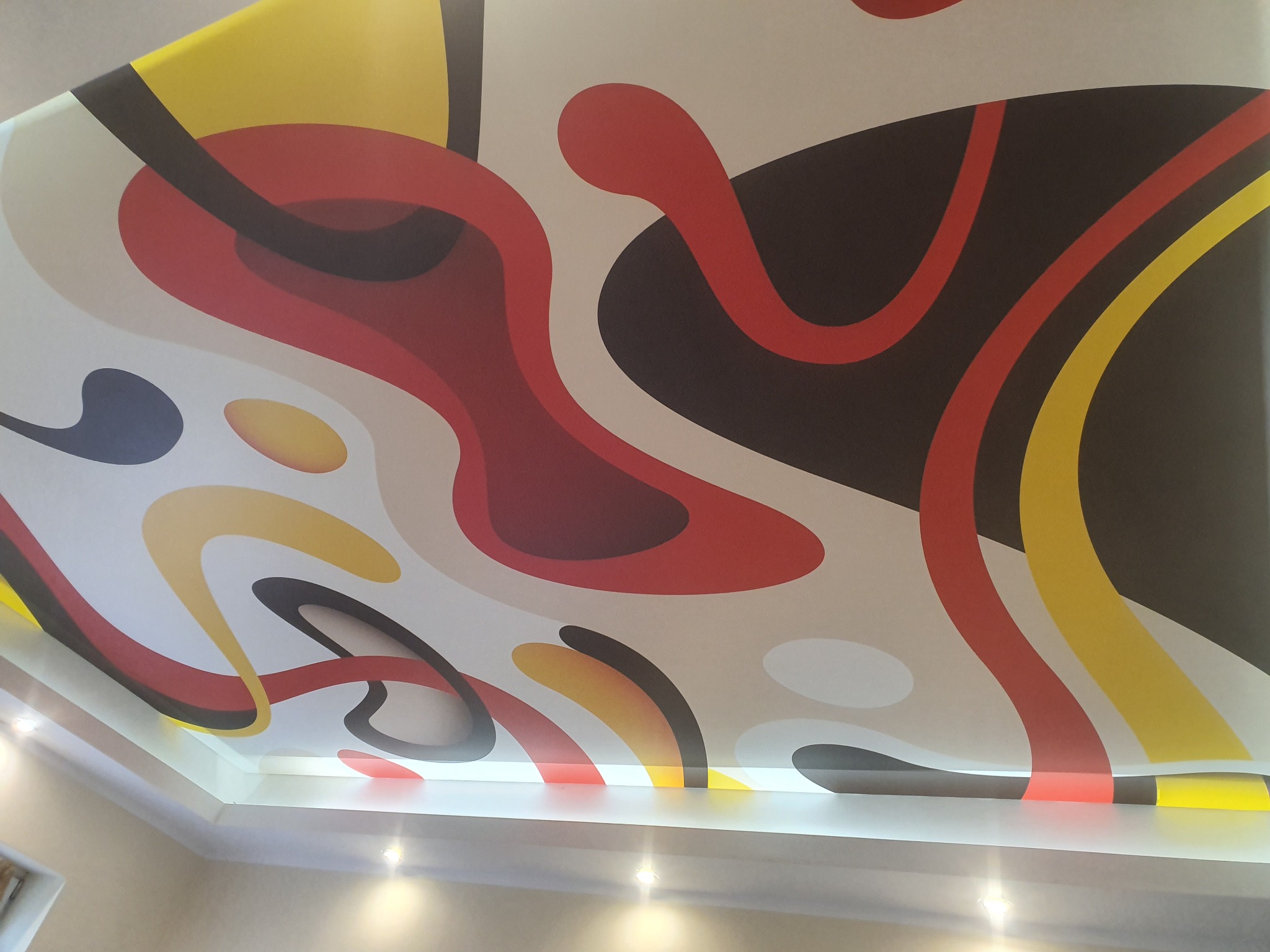 Abstrakcyjny wzór w kolorach czerwonym, żółtym i czarnym na suficie podwieszanym z oświetleniem punktowym LED.