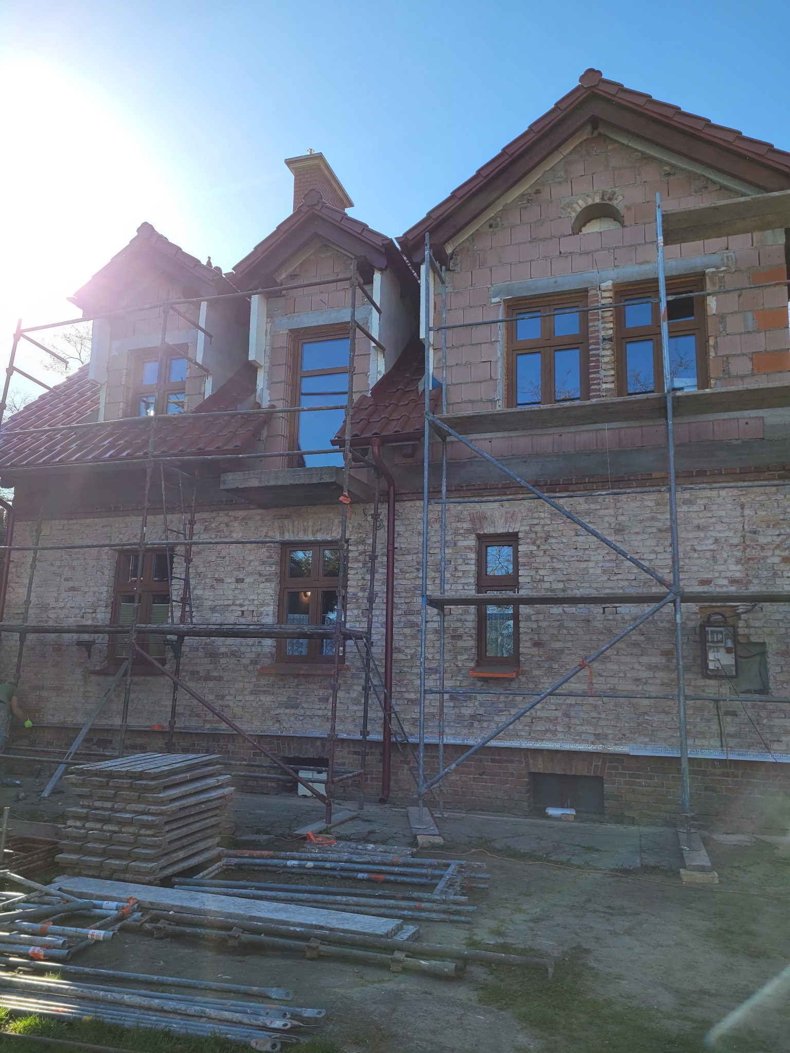 Dom w trakcie prac elewacyjnych, widoczne rusztowania, ceglana elewacja w trakcie budowy, nowe okna, dachówka ceramiczna.