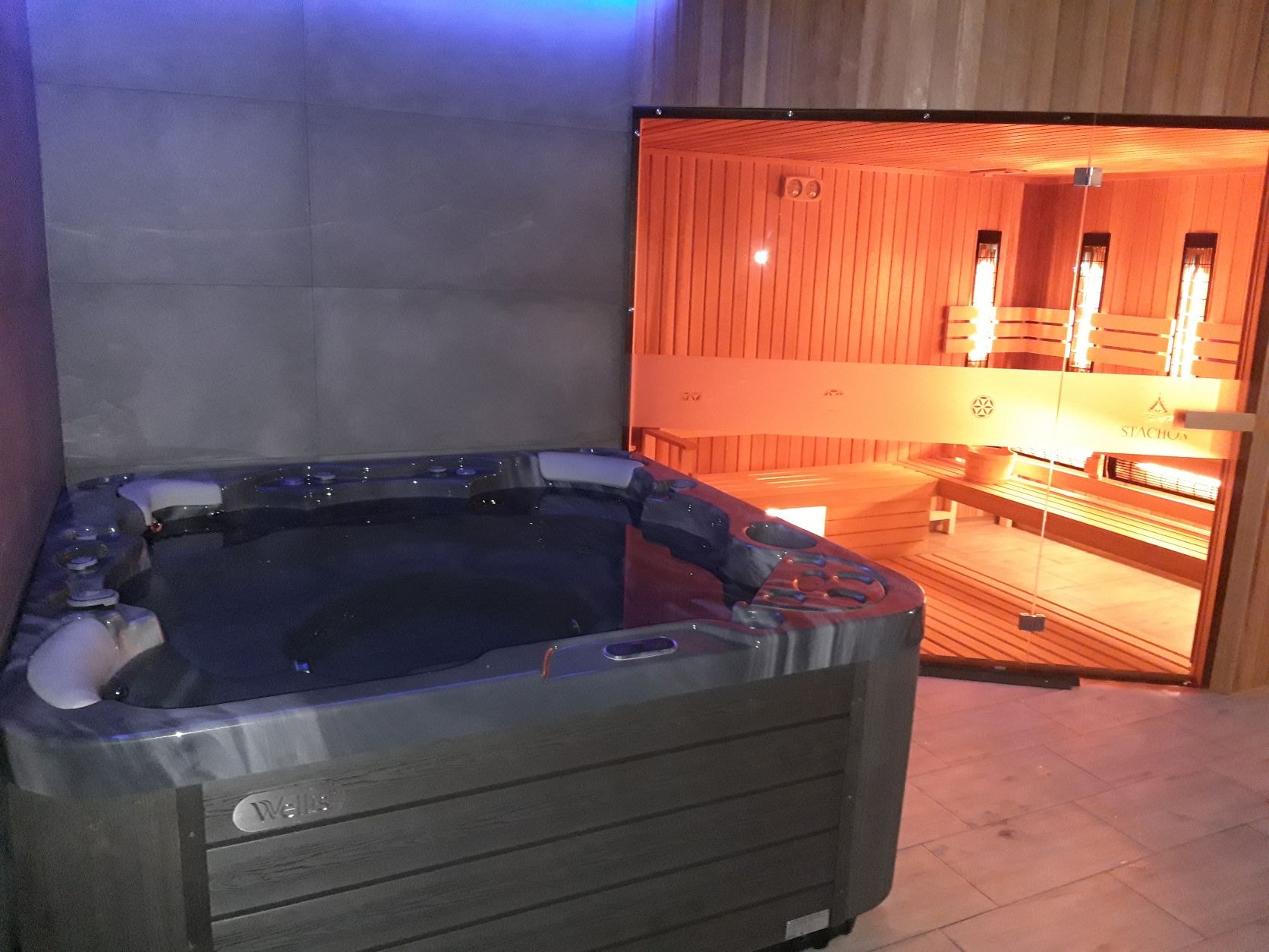 Nowoczesna wanna SPA z hydromasażem obok sauny z drewnianymi ławkami i grzejnikami na podczerwień, oświetlenie LED w kolorze niebieskim.